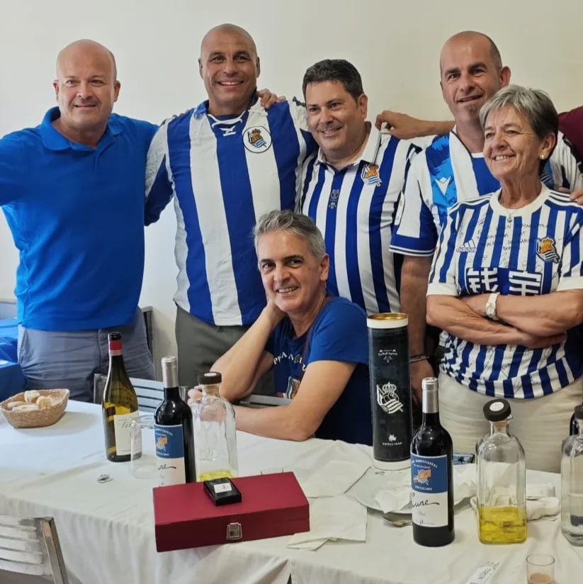 Socios posando junto a una mesa con vino y licores de la peña durante la comida del 10º aniversario