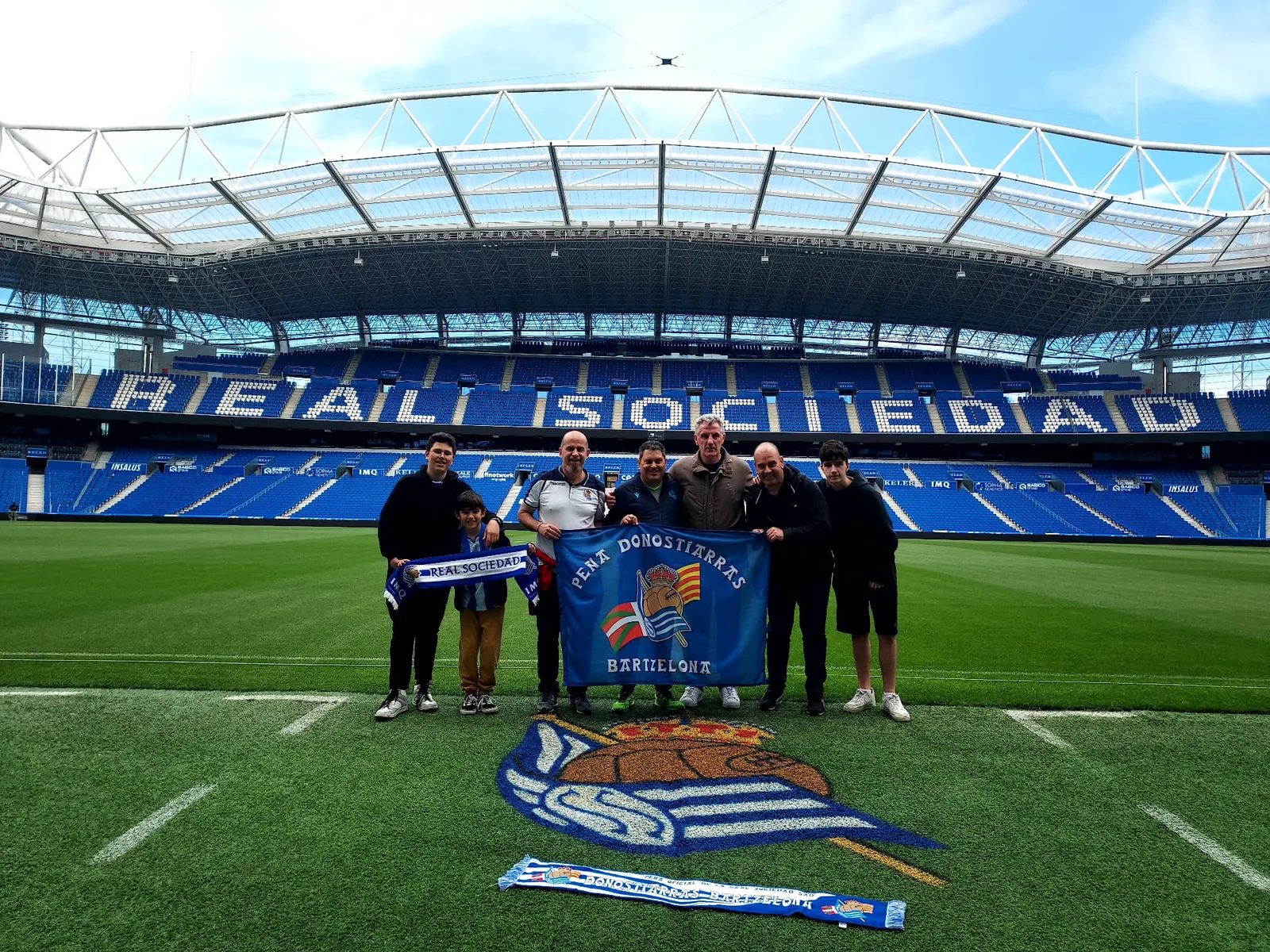 Grupo de socios con la bandera de la Peña Donostiarras Bartzelona sobre el césped del Reale Arena