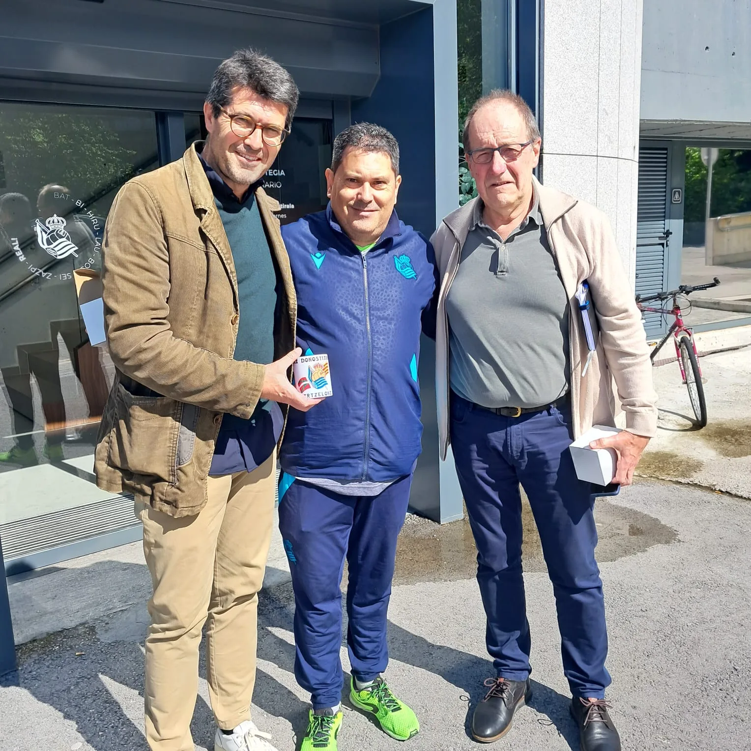 Socios de la peña en la calle ante las oficinas de la Real Sociedad con una taza de la peña