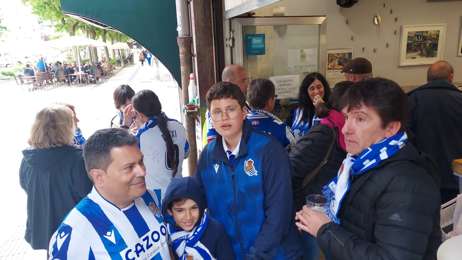 Grupo de socios, incluidos niños, en la entrada de un bar de Donostia antes del partido