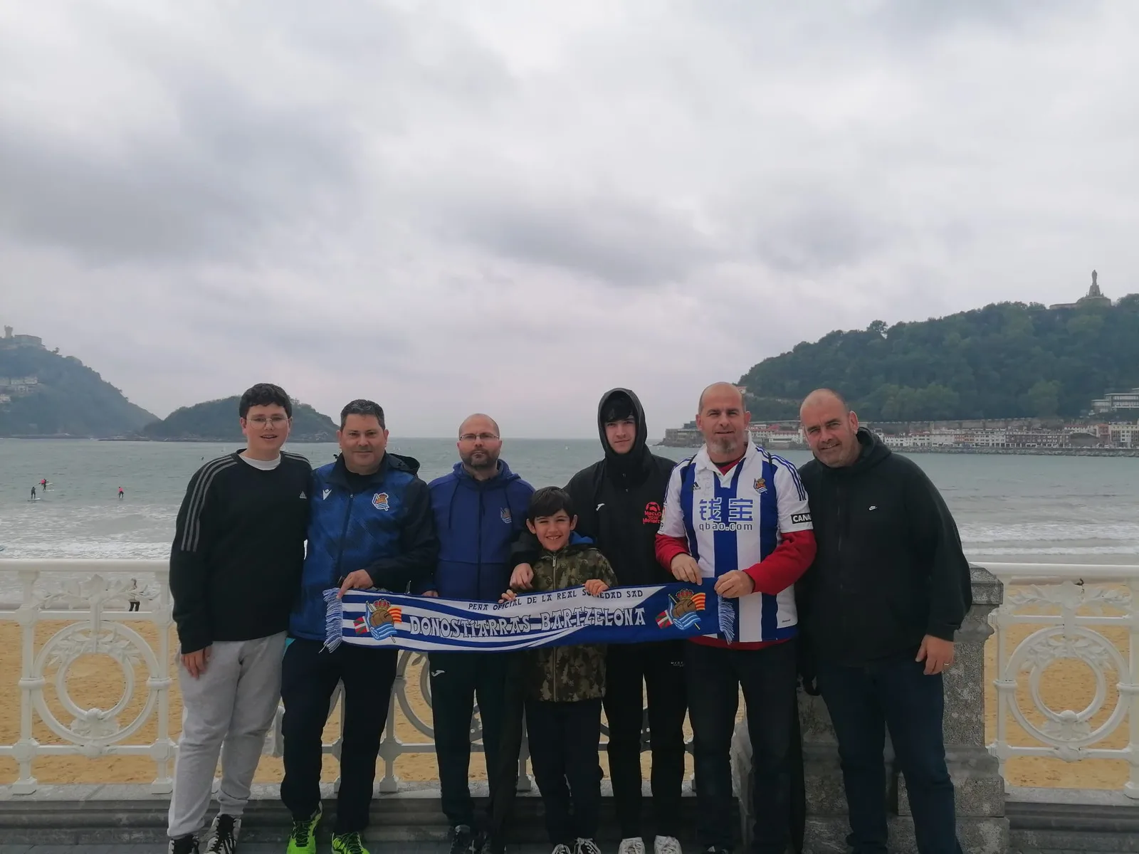 Socios de la peña con la bufanda Donostiarras Bartzelona en el paseo de La Concha, con la bahía al fondo