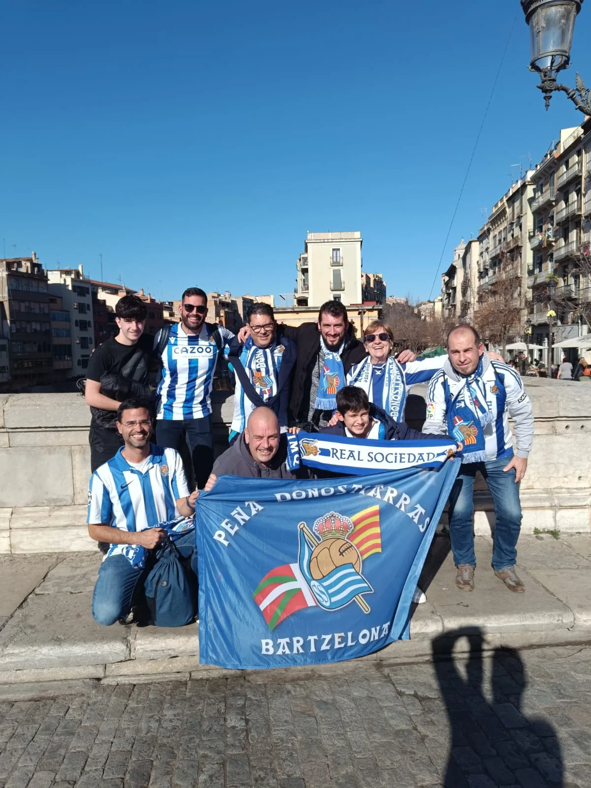 Socios con la bandera de la peña y una bufanda de la Real Sociedad en un puente sobre el río Onyar en Girona