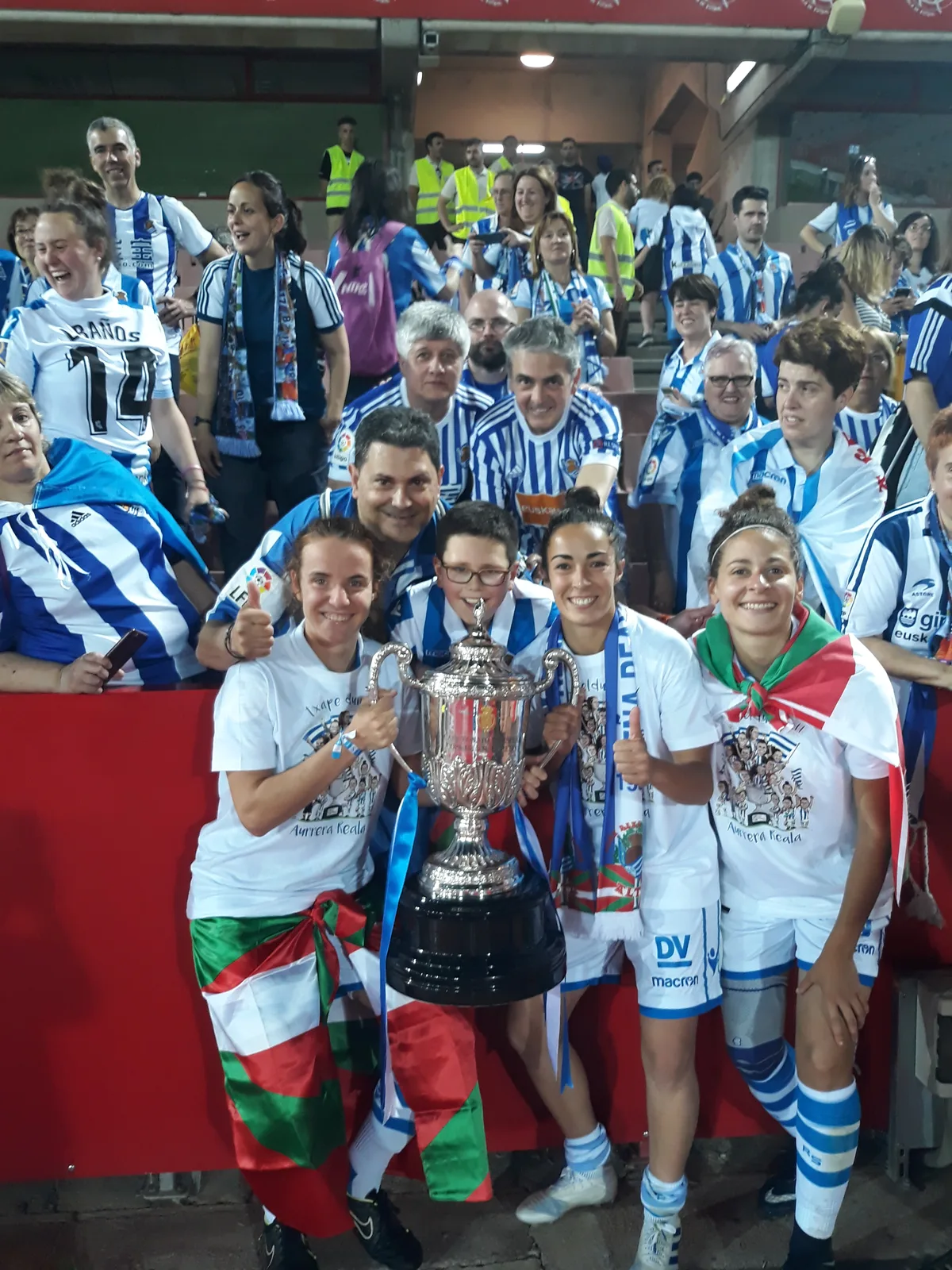 Familia de la peña posando con el trofeo de la Copa de la Reina junto a jugadoras de la Real Sociedad