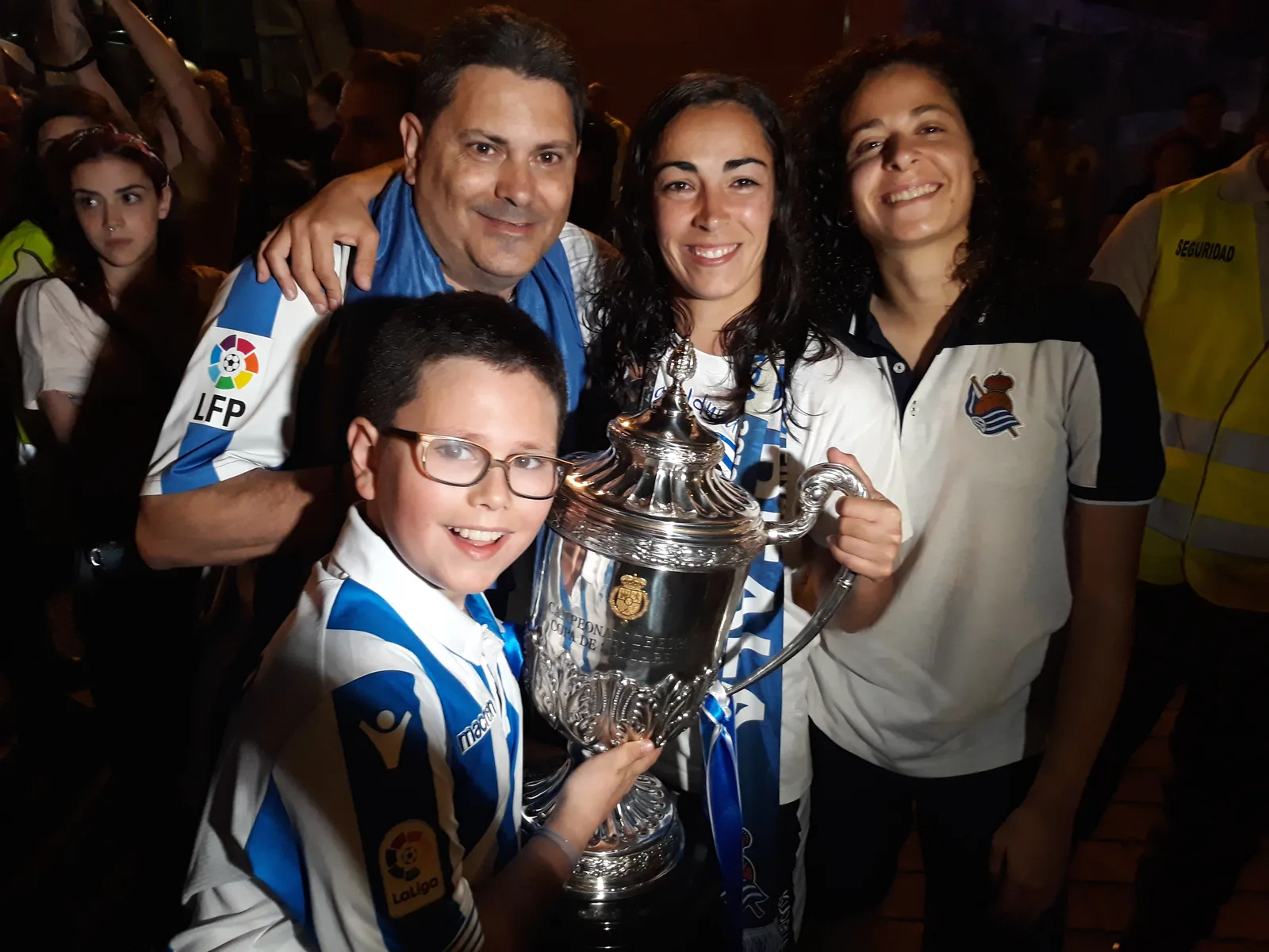 Familia de la peña con el trofeo de la Copa de la Reina de cerca, junto a una jugadora de la Real Sociedad