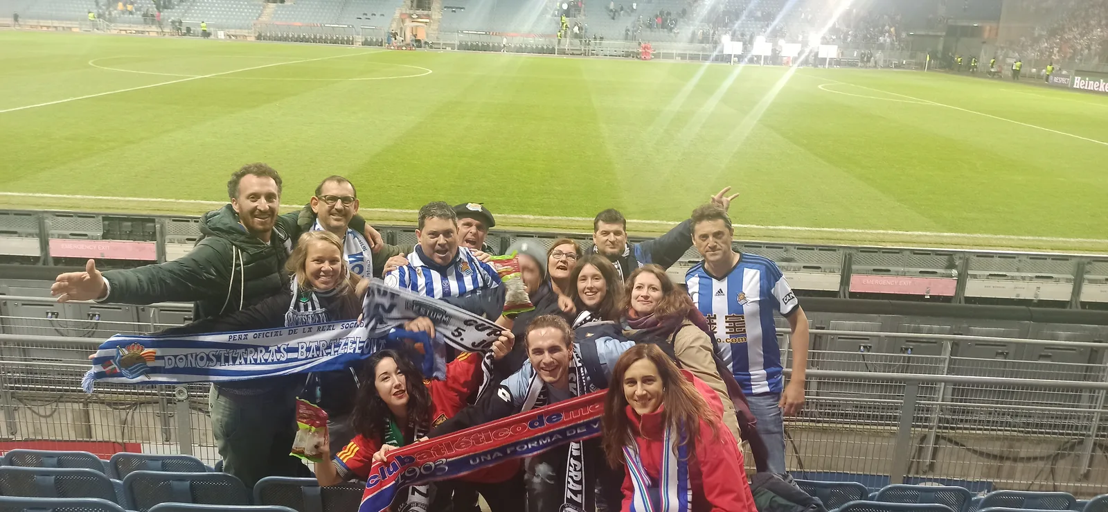 Grupo numeroso de socios en la grada del estadio de Graz de noche con bufandas de la Real Sociedad