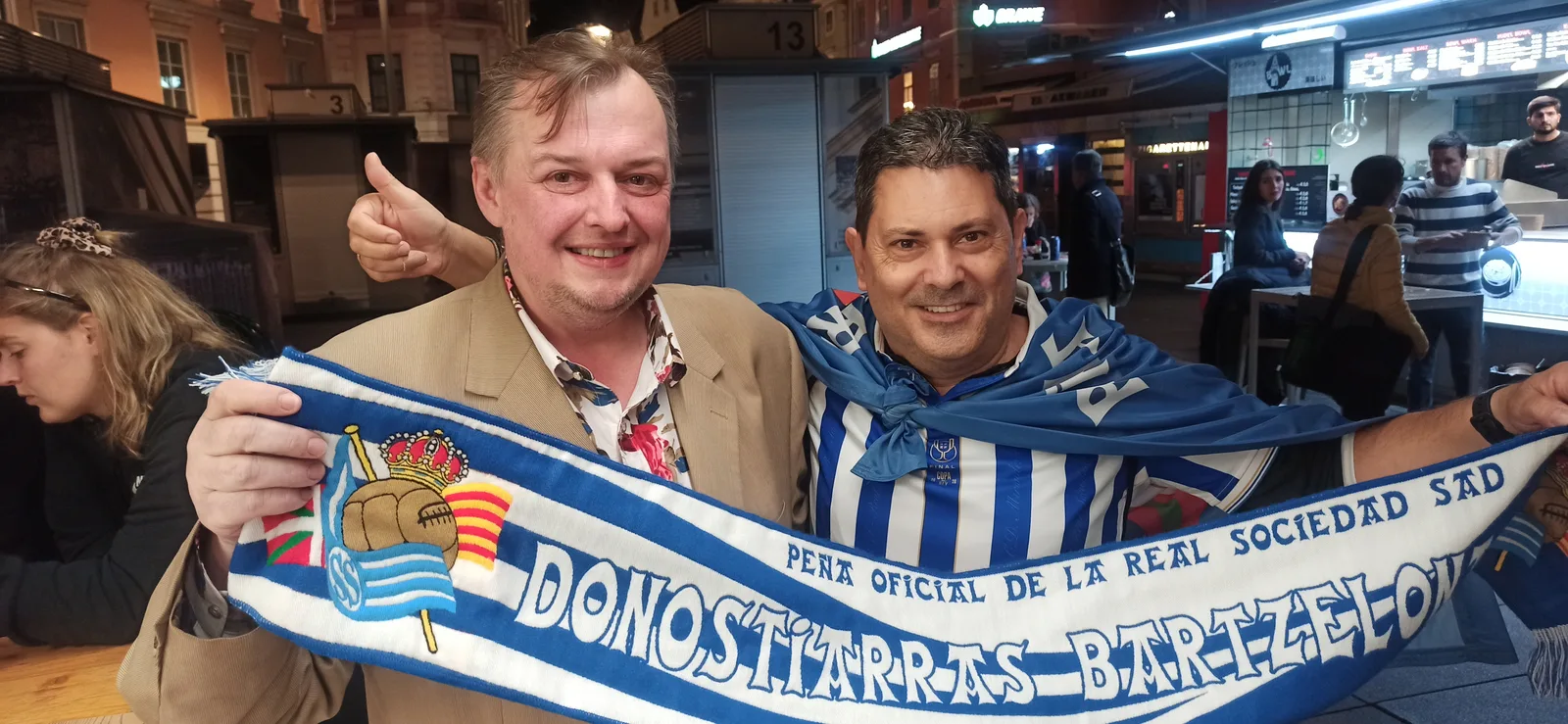 Dos socios de la peña con la bufanda Donostiarras Bartzelona en una plaza de Graz de noche