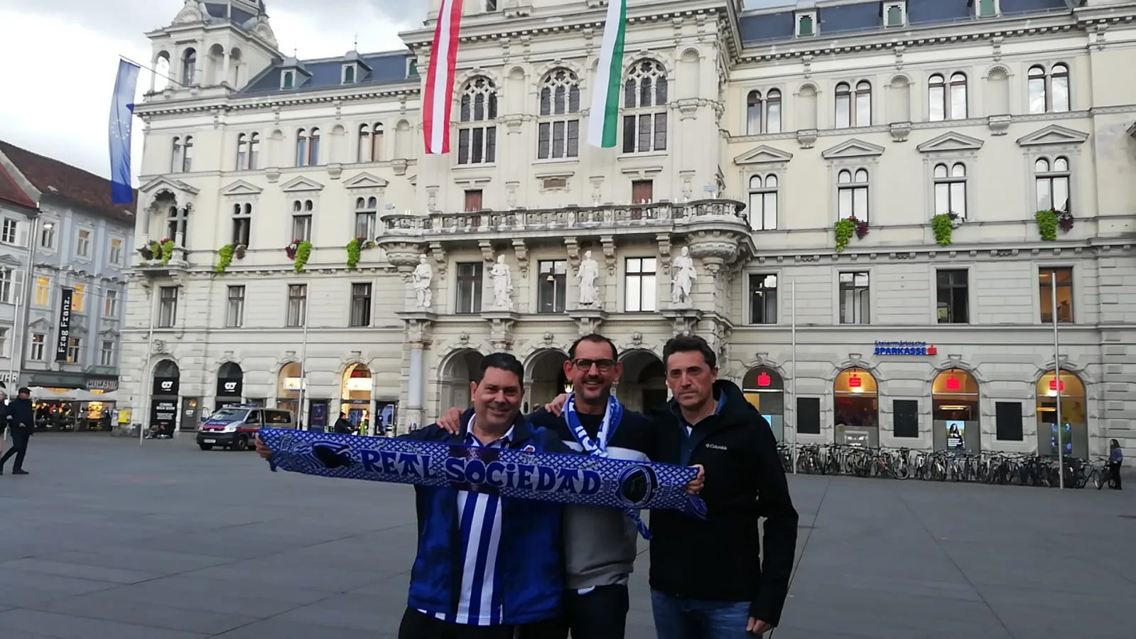 Socios de la peña con la bufanda de la Real Sociedad ante el ayuntamiento de Graz (Rathaus), de día