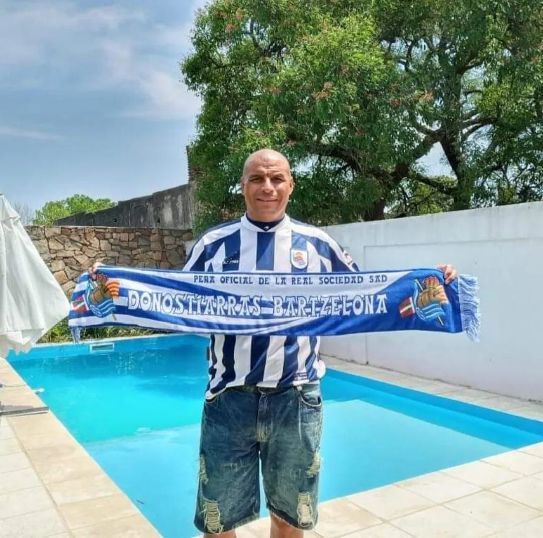 Socio de la peña con la bufanda Donostiarras Bartzelona extendida junto a una piscina