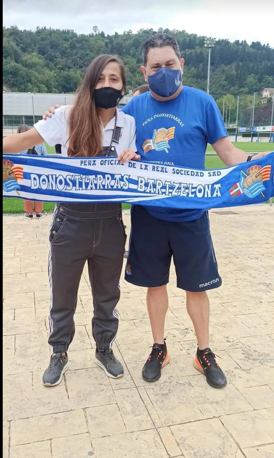 Jugadora de la Real Sociedad femenina y socio de la peña sujetando la bufanda en un campo de entrenamiento
