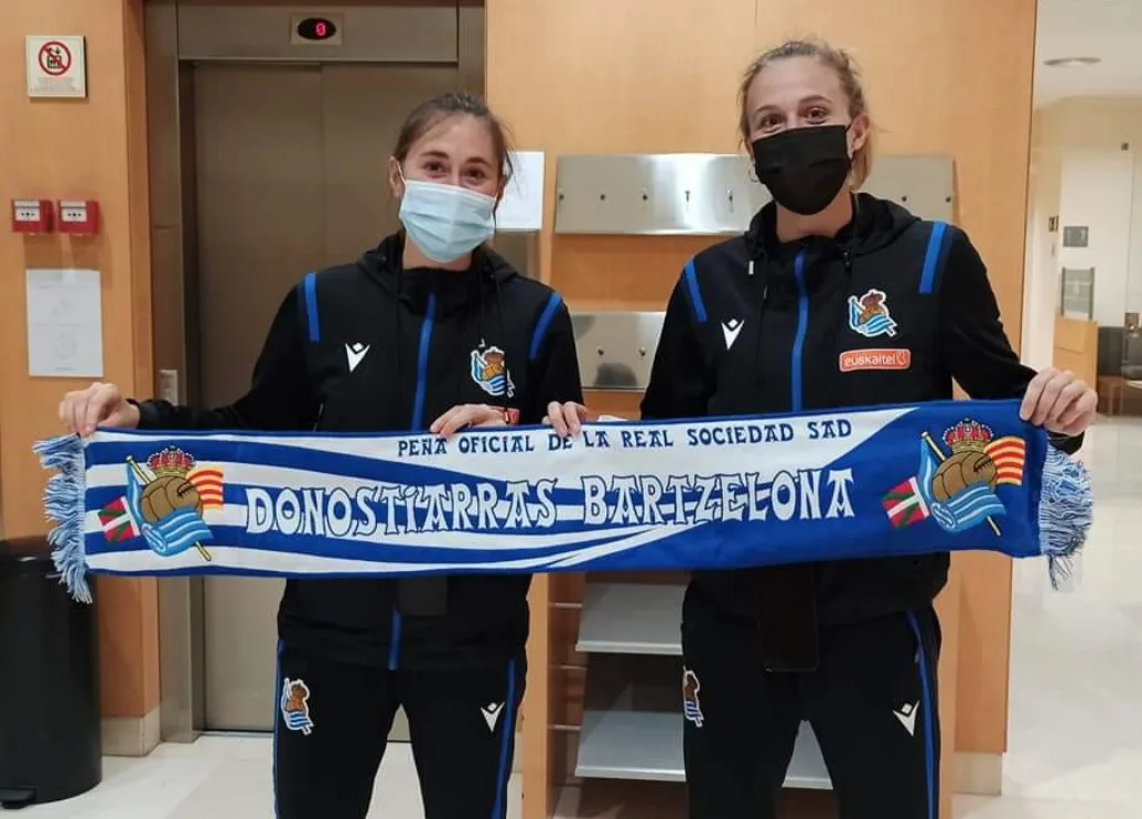 Dos jugadoras de la Real Sociedad femenina sujetando la bufanda de la peña junto a un ascensor de hotel