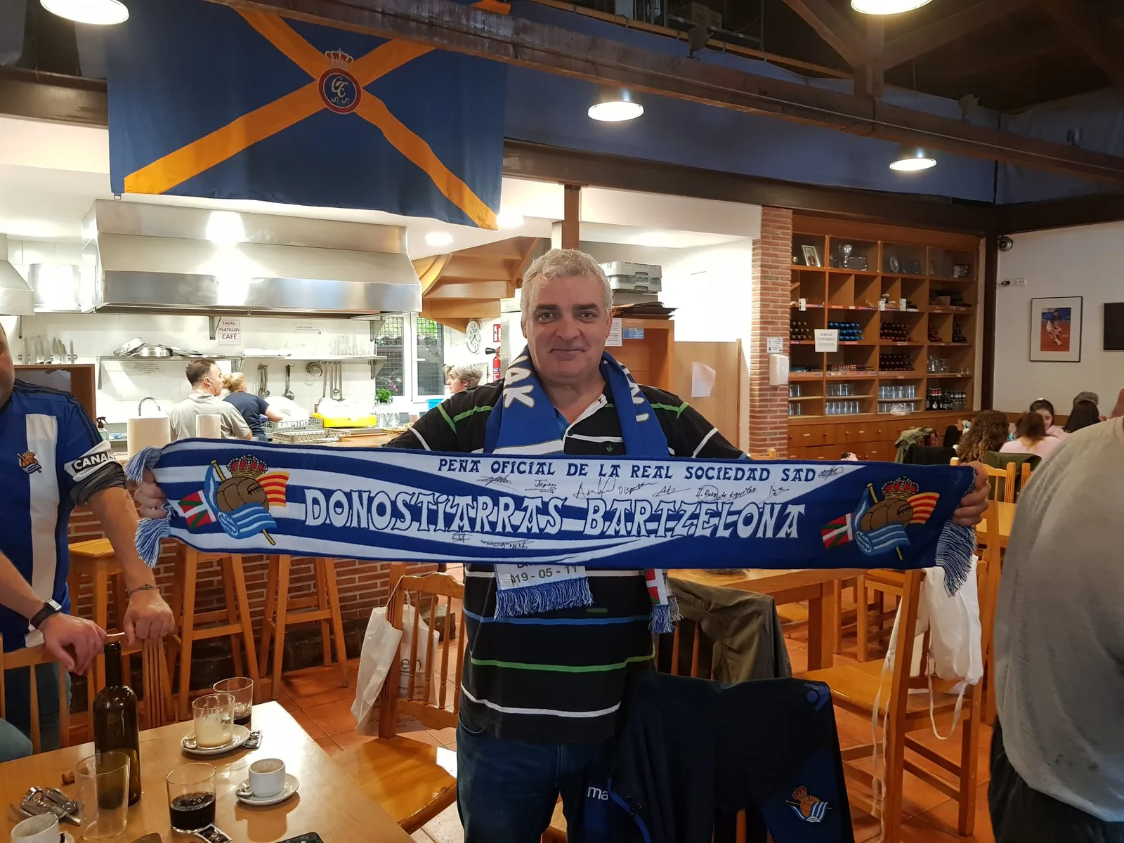 Socio con la bufanda de la peña llena de firmas en el interior de un restaurante con la bandera del Celta de Vigo