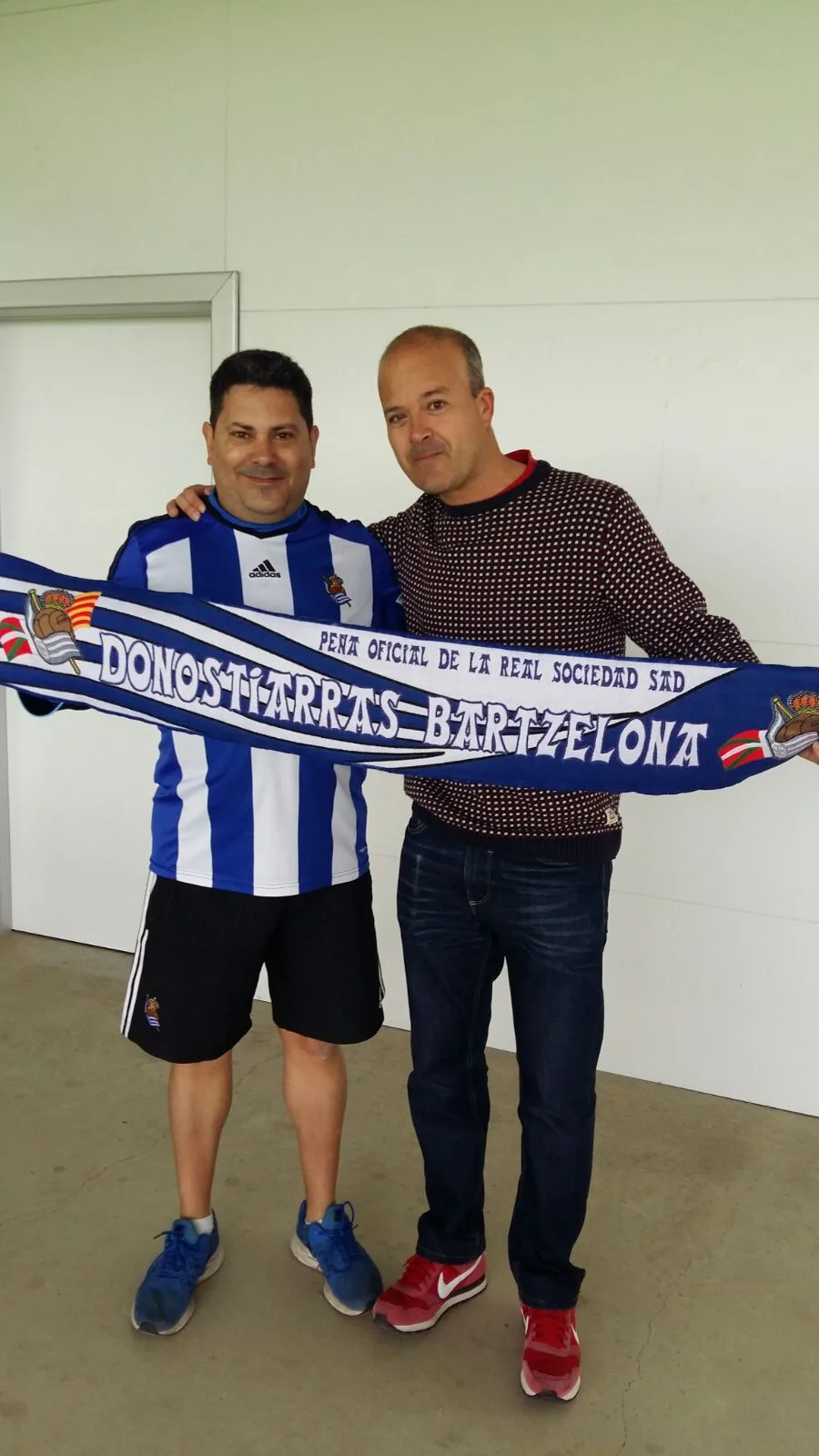 Dos socios de la peña posando juntos con la bufanda Donostiarras Bartzelona en un interior