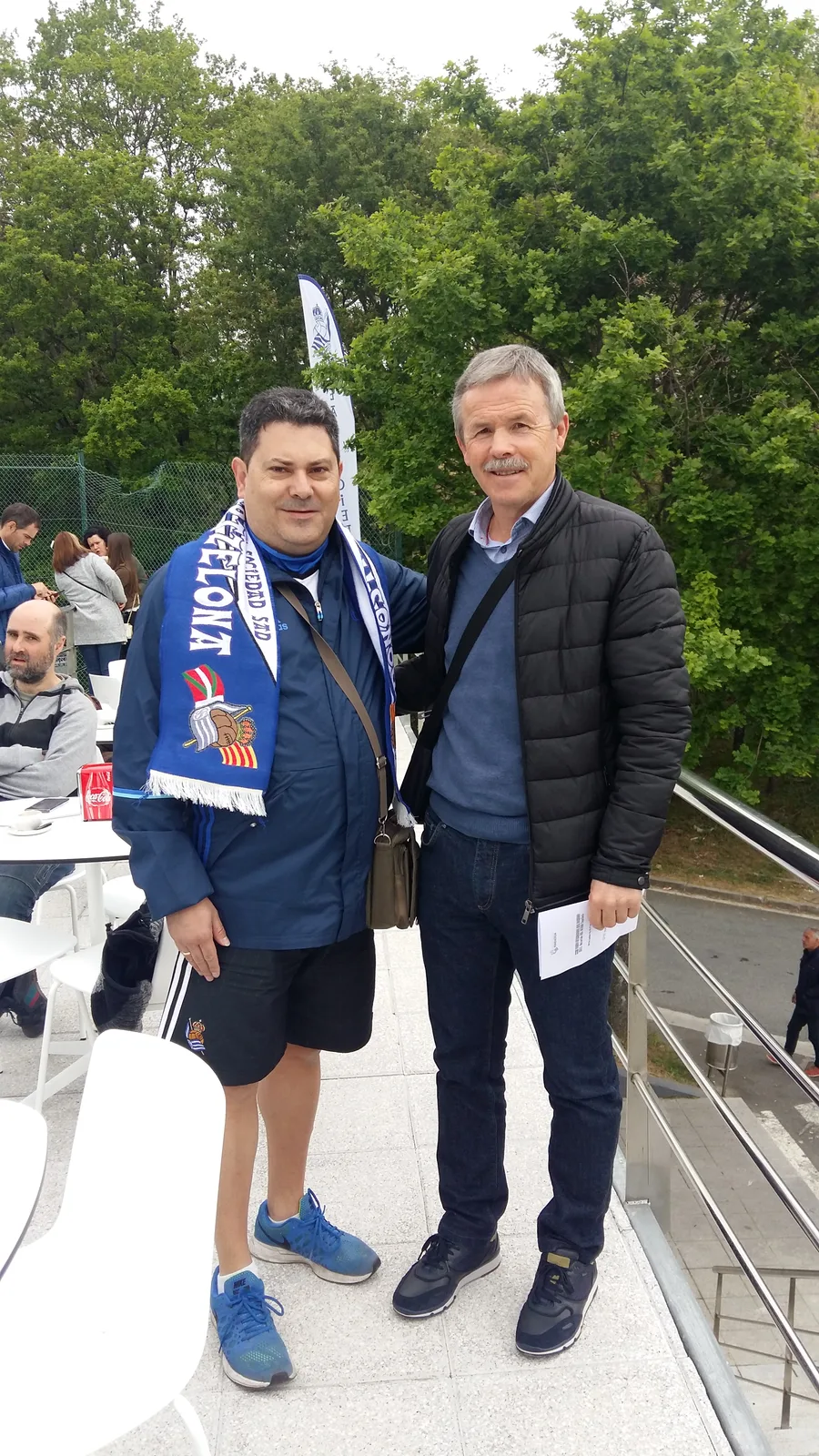 Dos socios de la peña con la bufanda Donostiarras Bartzelona en una terraza exterior