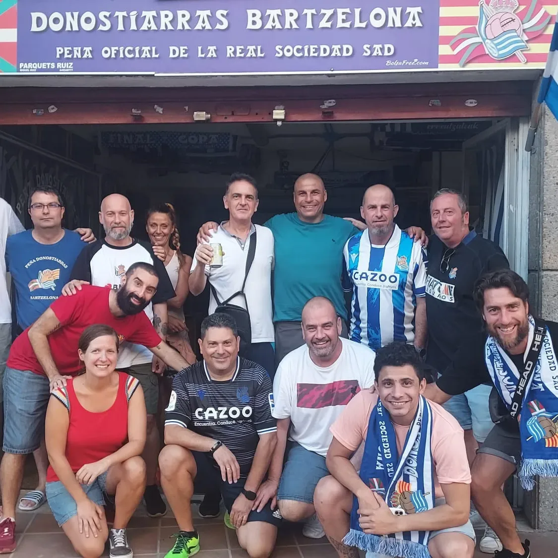Socios de la Peña Donostiarras Bartzelona posando bajo el rótulo de su local en Barcelona