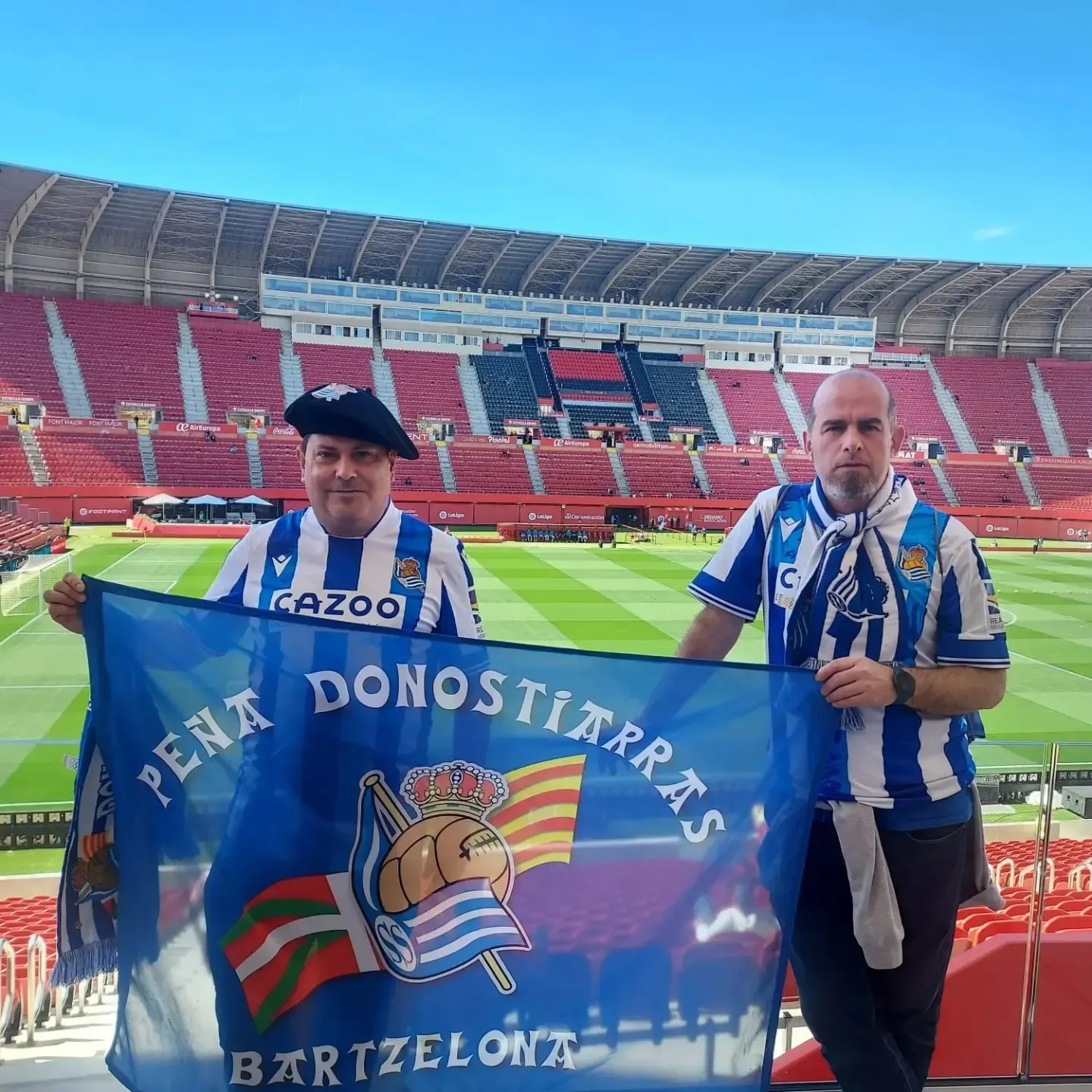 Socios de la peña con boina desplegando la bandera de la Peña Donostiarras Bartzelona en el Son Moix de Mallorca