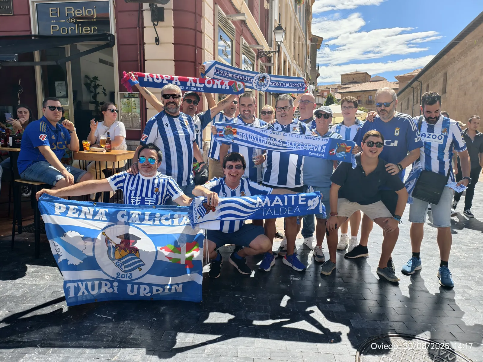 Grupo numeroso de socios en una calle de Oviedo con banderas y bufandas de varias peñas de la Real Sociedad