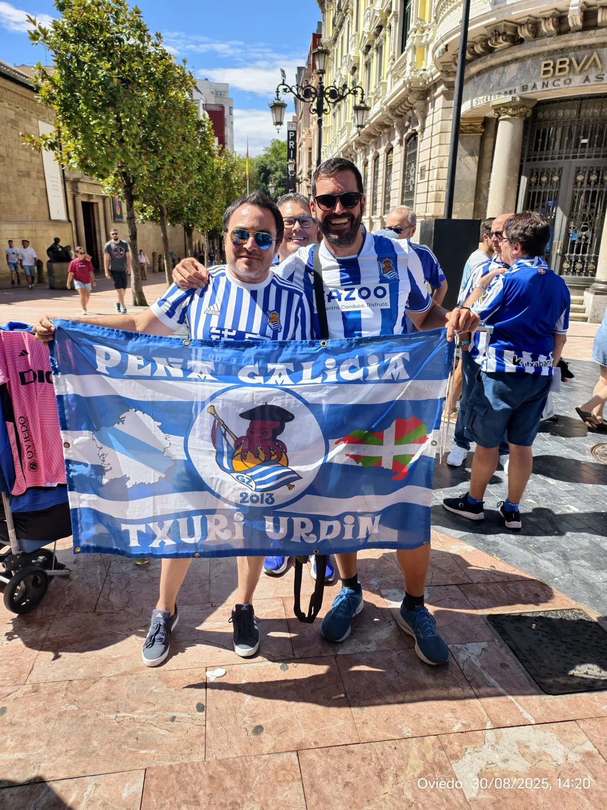 Socios con la bandera de la Peña Galicia Txuri Urdin en una calle histórica de Oviedo