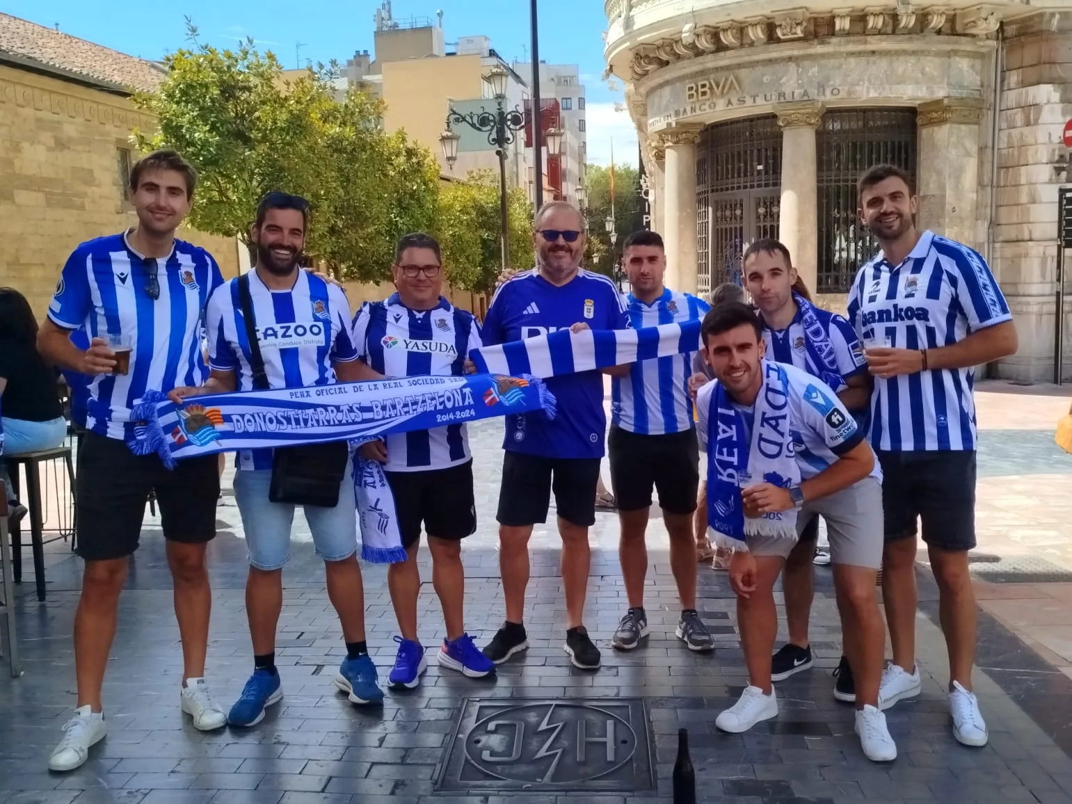 Socios de la peña con la bufanda Donostiarras Bartzelona junto a un edificio histórico de Oviedo