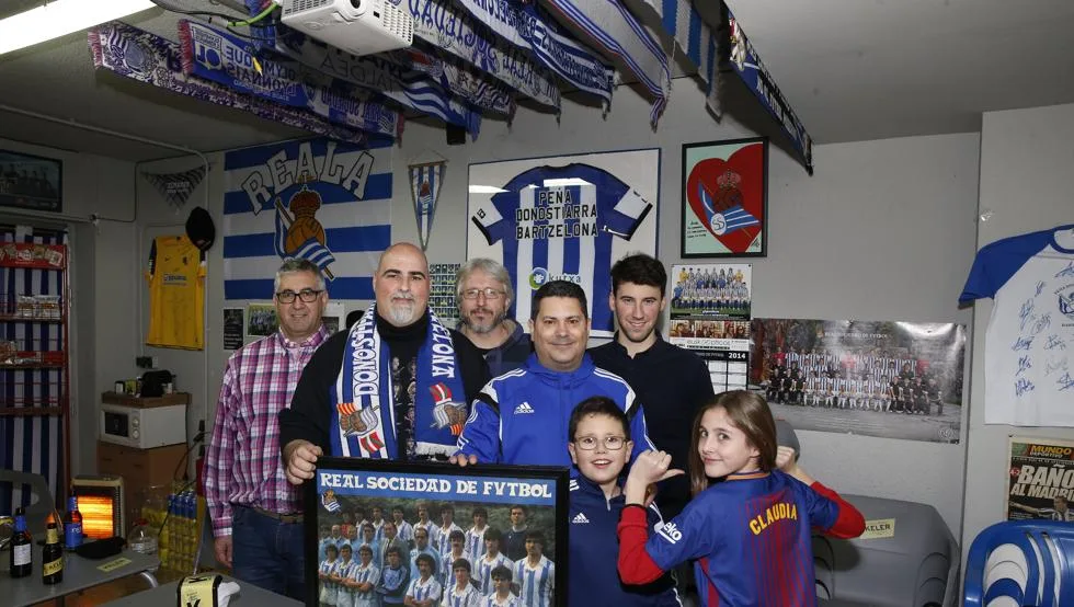 Socios de la peña en el local mostrando un póster histórico de la Real Sociedad